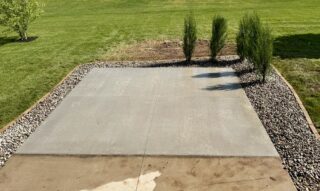 New concrete patio with decorative stone border and privacy shrubs